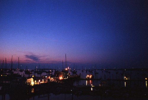 A serene harbor at dusk, with boats docked and a colorful sky transitioning from blue to purple.