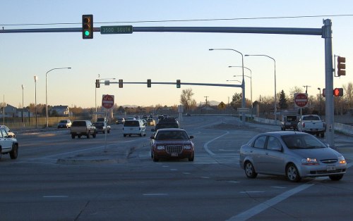 Traffic at an intersection with a green light, stop signs, and vehicles on the road during early evening.
