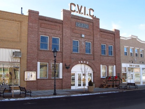 Historic brick building with "C.V.I.C." sign, featuring large front windows and decorative elements, set in a snowy street.