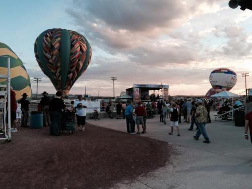 A lively outdoor event with colorful hot air balloons and a crowd enjoying the festivities under a cloudy sky.