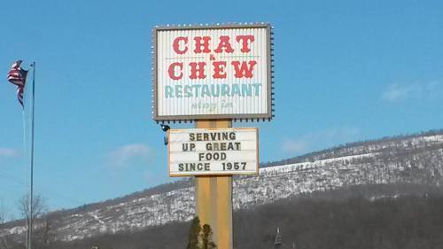 Sign for Chat & Chew Restaurant, featuring "Serving Up Great Food Since 1957," with a snowy mountain backdrop.
