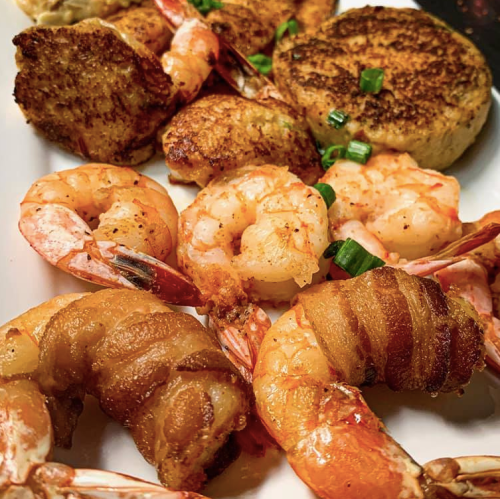 A close-up of a plate featuring shrimp, crab cakes, and garnished with green onions.