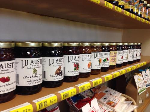 A shelf displaying various jars of jam with labels, including flavors like blackberry, cherry, and peach.