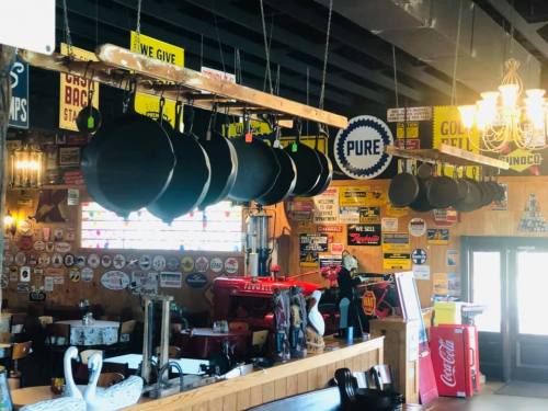A rustic restaurant interior with hanging pots, vintage signs, and wooden decor, creating a cozy atmosphere.