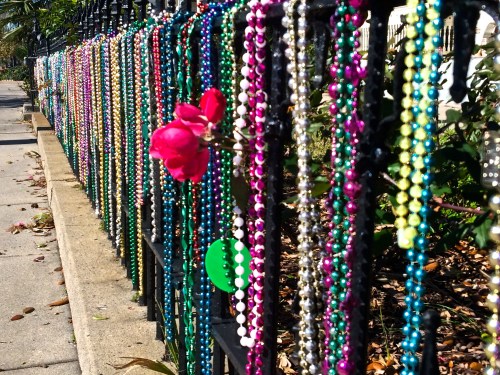 Colorful beads hang on a black fence, with a bright pink flower adding a pop of color among the decorations.