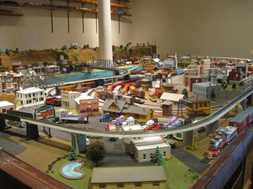 A detailed model train layout featuring buildings, vehicles, and tracks in a scenic miniature landscape.