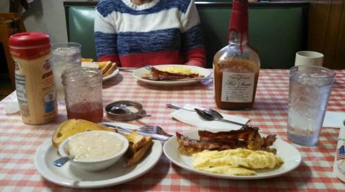 A breakfast spread with eggs, bacon, toast, grits, and drinks on a checkered tablecloth.