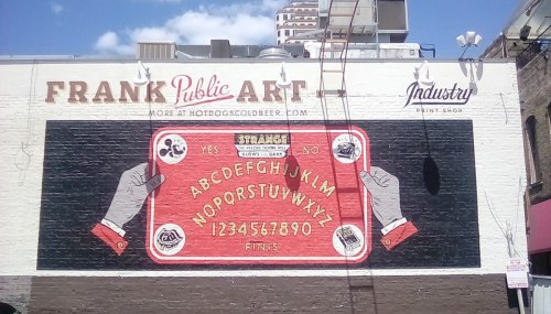 Mural featuring a vintage-style design with letters, numbers, and the text "STRANGE NO" on a brick wall.
