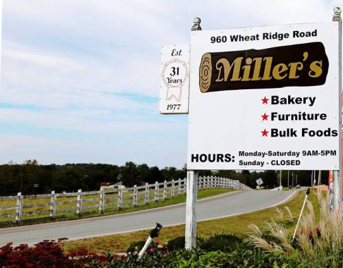 Sign for Miller's at 960 Wheat Ridge Road, featuring bakery, furniture, and bulk foods. Open Monday-Saturday, closed Sunday.