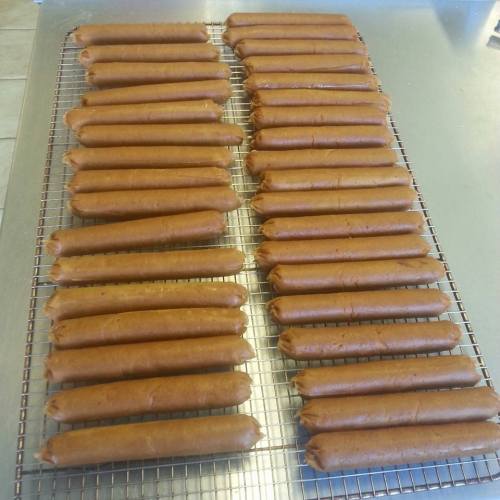 A tray of neatly arranged, uncooked hot dog sausages cooling on a wire rack.