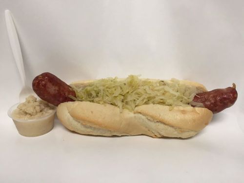 A hot dog in a bun topped with sauerkraut, served with a side of sauerkraut in a small cup.