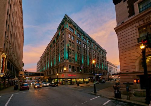 Historic building with teal lighting at dusk, located at a busy intersection with cars and streetlights.