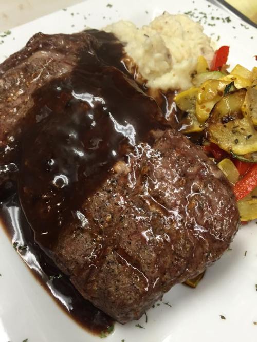 A plate featuring sliced meatloaf with gravy, mashed potatoes, and sautéed vegetables.