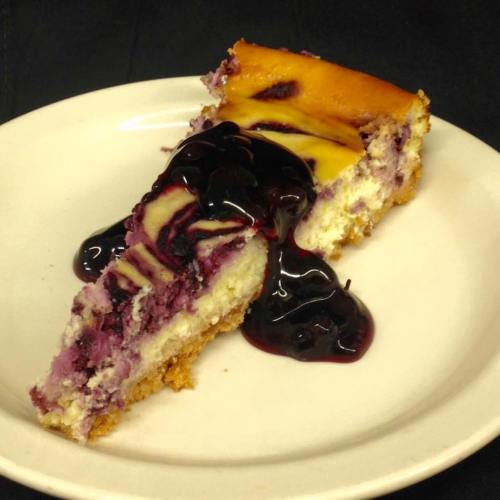 A slice of cheesecake topped with blueberry sauce on a white plate.