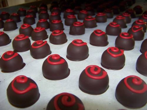 A close-up of rows of chocolate truffles with red swirls on top, arranged neatly on parchment paper.