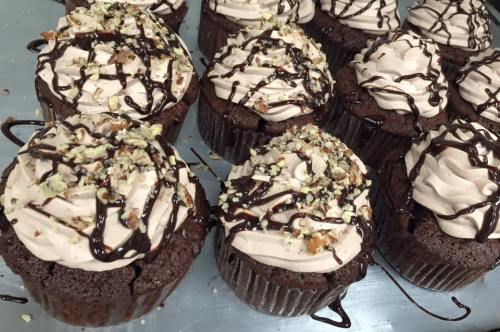 Delicious chocolate cupcakes topped with swirls of frosting, drizzled with chocolate and sprinkled with nuts.
