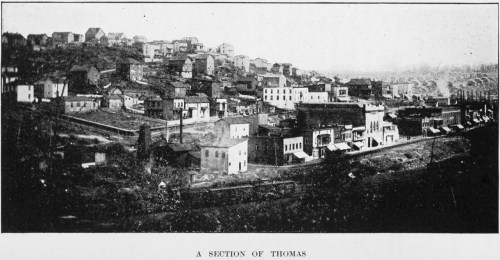 A faded historical image of a town section, featuring buildings and hills in the background.