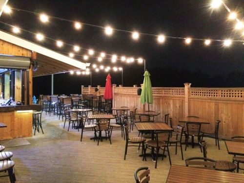 Outdoor dining area at night, featuring string lights, empty tables, and colorful umbrellas.