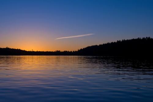 A serene lake at sunset, reflecting vibrant colors in the water, with a silhouette of trees along the horizon.