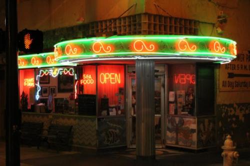 A brightly lit seafood restaurant with neon signs reading "OPEN" and "SEA FOOD" at night.