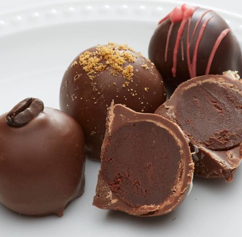 A plate of assorted chocolate truffles, including one cut in half to reveal a creamy filling.