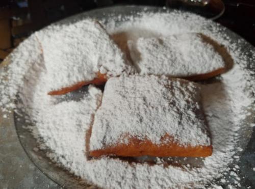 A plate of three powdered sugar-covered pastries, resting on a silver platter.