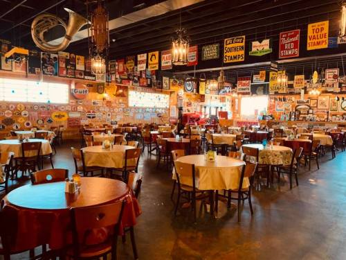 A cozy restaurant interior with round tables, vintage signs on the walls, and warm lighting.
