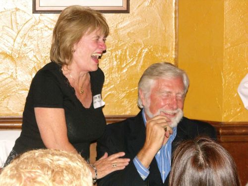 A woman laughs joyfully while playfully touching a man's shoulder, both enjoying a lighthearted moment together.