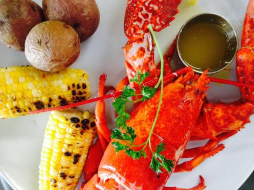 A plate featuring a cooked lobster, corn on the cob, boiled potatoes, and a small cup of melted butter.
