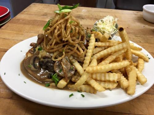 A plate of crispy fries, topped with a savory dish of meat, gravy, mushrooms, and crispy onion strings, garnished with green onions.
