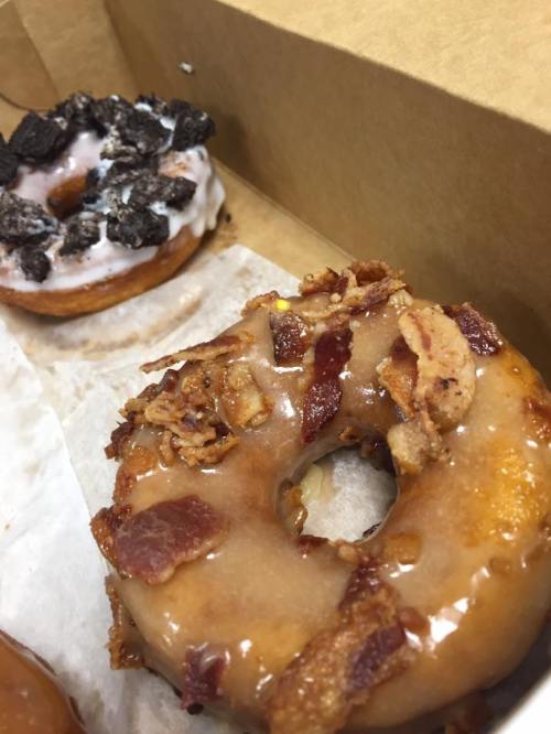 A close-up of two donuts: one topped with bacon and glaze, the other with cookies and cream icing.