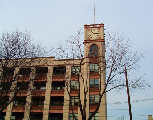 A clock tower atop a multi-story building, with bare trees in the foreground and a cloudy sky.