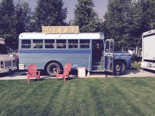 A blue vintage bus converted into a coffee shop, parked on grass with two red chairs in front and a sign that says "COFFEE."