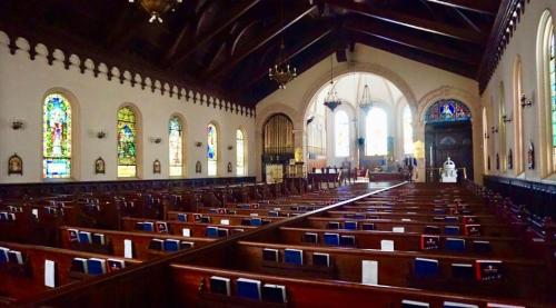 Interior of a church featuring wooden pews, stained glass windows, and a high ceiling with chandeliers.