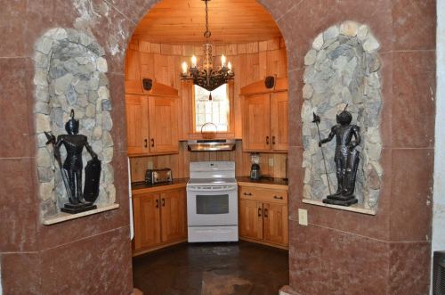 A cozy kitchen with wooden cabinets, stone accents, and two decorative statues flanking an archway.