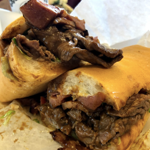 A close-up of a hearty sandwich filled with sliced beef, bacon, and lettuce, served in a toasted bun.