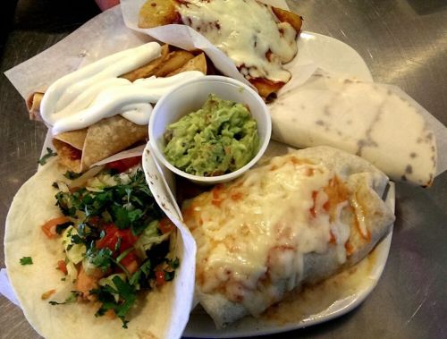 A plate of Mexican food featuring tacos, burritos, guacamole, and cheese-covered enchiladas.