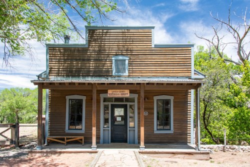 Historic wooden building with a porch, large windows, and a sign reading "Jasper County Courthouse." Surrounded by trees.