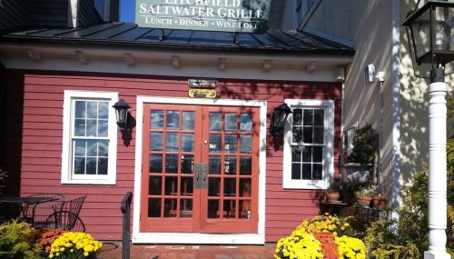 A charming red building with double doors, surrounded by colorful flower pots and outdoor seating.