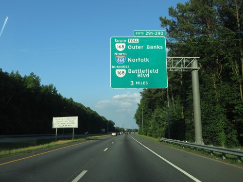 Highway sign indicating directions to Outer Banks, Norfolk, and Battlefield Blvd, with a clear blue sky in the background.