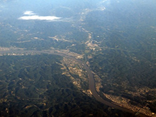 Aerial view of a winding river surrounded by lush green hills and a small town along the riverbank.
