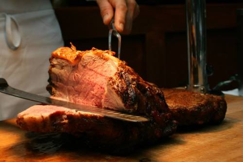 A chef slices a large, juicy roast on a wooden cutting board, showcasing its tender pink interior.
