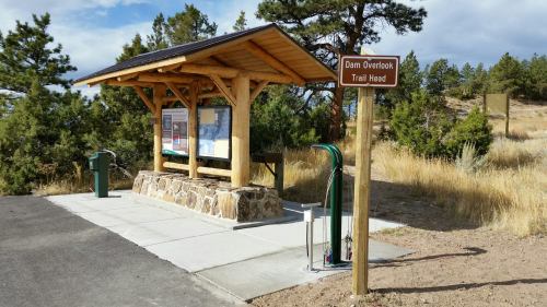 A wooden shelter at a trailhead with informational signs, surrounded by trees and open land.