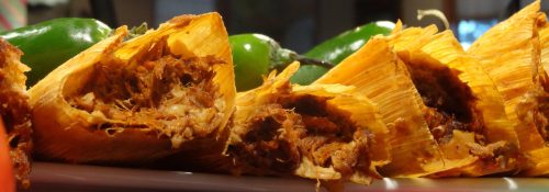 A close-up of tamales filled with shredded meat, surrounded by green jalapeños on a plate.