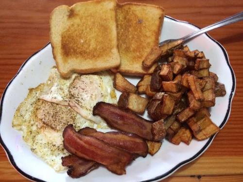 A plate of breakfast featuring two fried eggs, crispy bacon, toasted bread, and golden-brown diced potatoes.