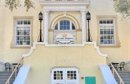 A charming yellow building with a sign for "Le Café Belge" and blooming flowers in front.