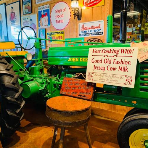 A vintage green John Deere tractor beside a wooden table with a sign about cooking with Jersey cow milk.