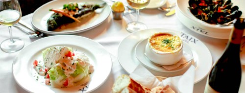 A table set with various dishes: salad, mussels, a creamy soup, and bread, accompanied by glasses of white wine.