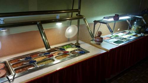 A buffet table with various dishes and toppings in metal trays, illuminated by overhead lights.