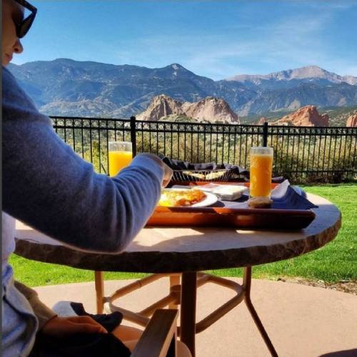 A person enjoys breakfast with orange juice, overlooking mountains and a scenic landscape.